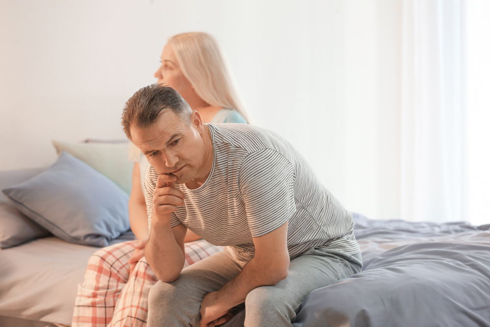 man sitting on bed thinking next to wife