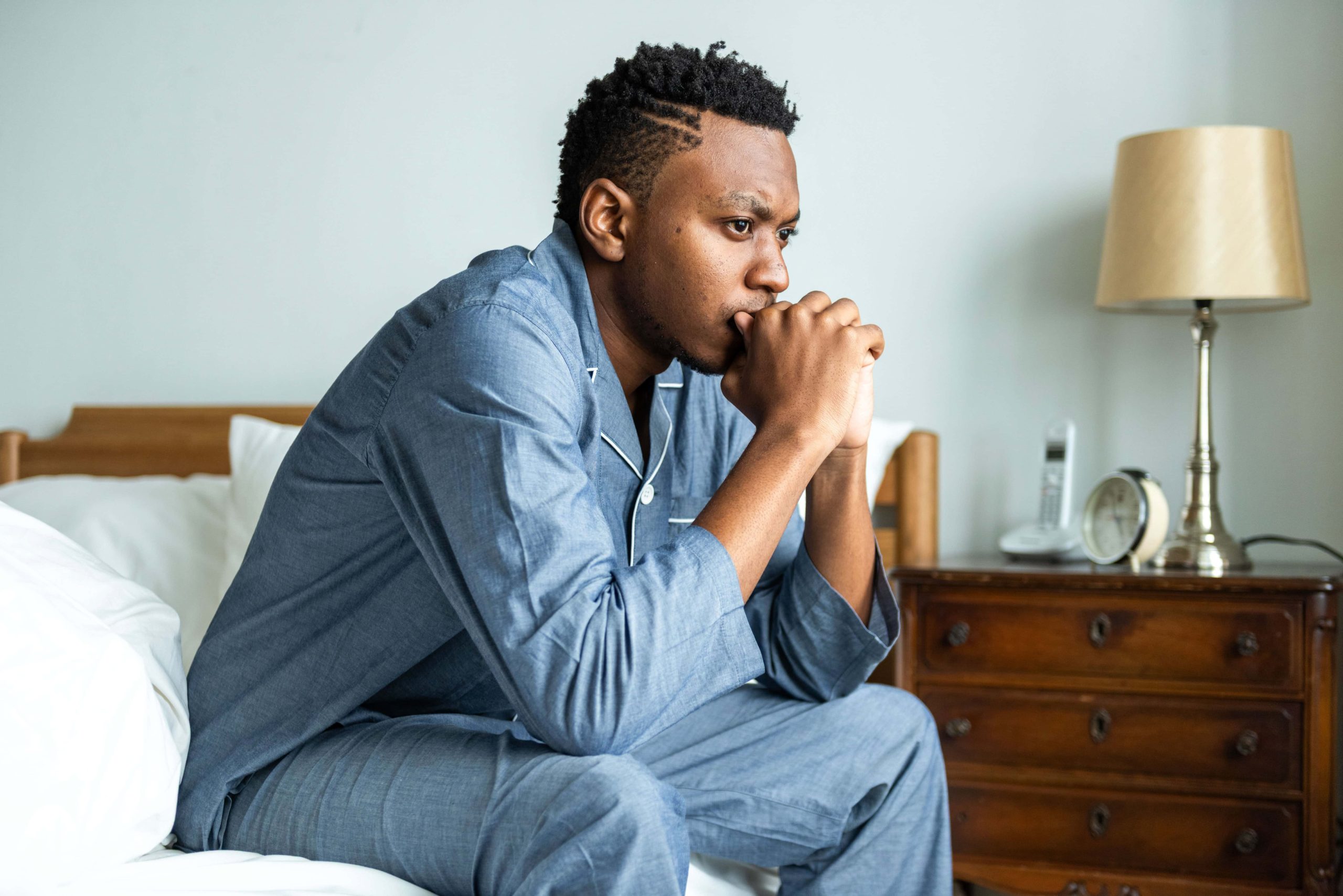 Man sitting on a bed looking concerned about erectile dysfunction