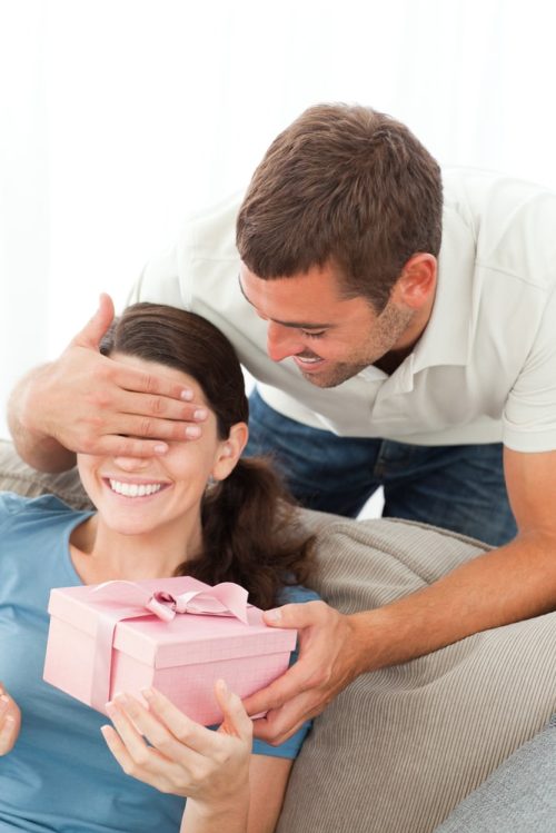 Man sneaking up from behind to surprise his wife with a gift